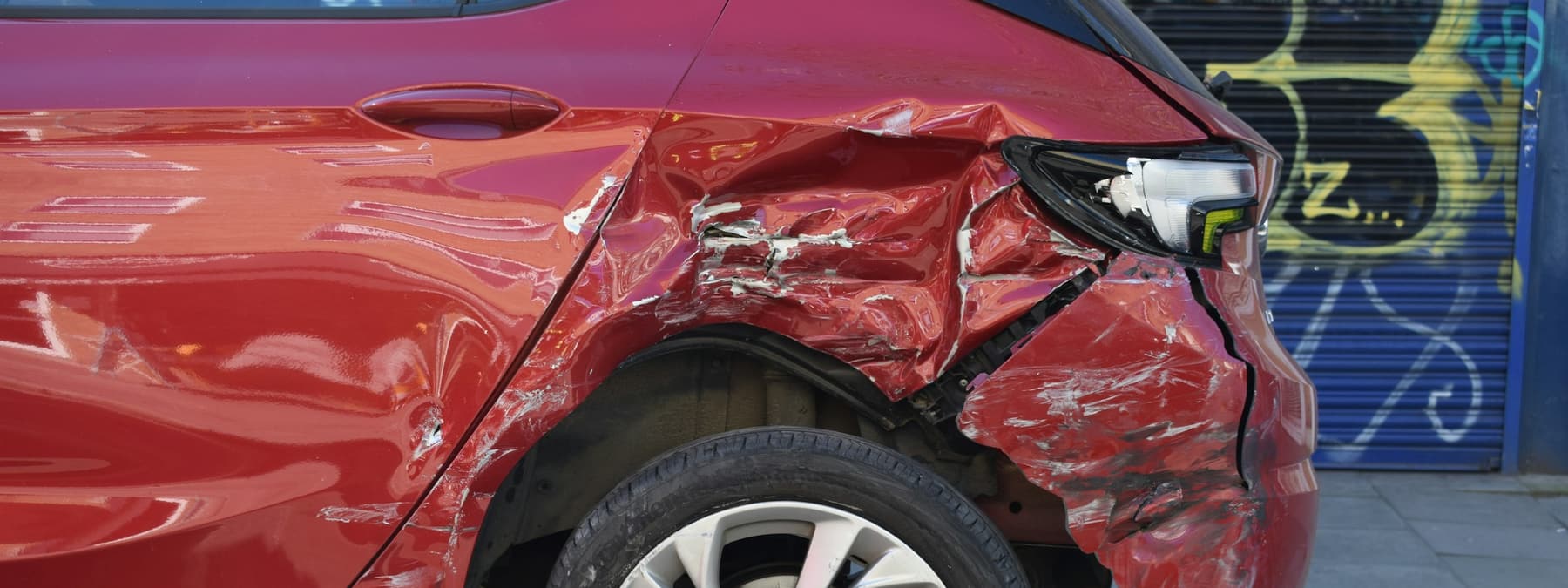 A red car with rear-quarter collision damage strapped to the bed of a flatbed recovery truck.