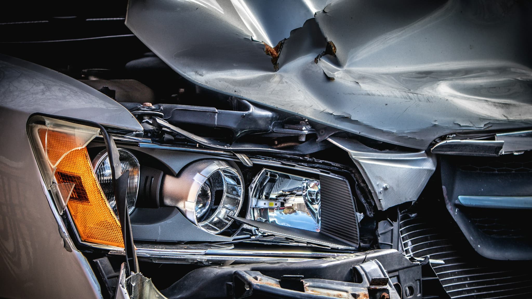Front-end collision damage to a modern car: a crumpled hood and a broken headlight assembly.